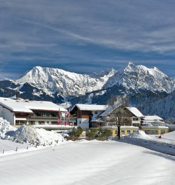 Die Außenansicht des Hotels Berwanger Hof in Obermaiselstein mit Bergpanorama im Winter