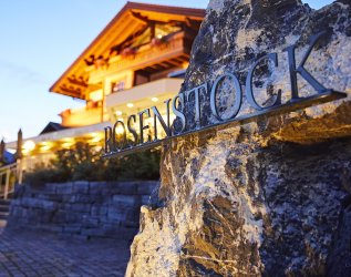 Hotellogo des Hotels Rosenstock in Fischen mit einem Teil des Hotelgebäudes im Hintergrund