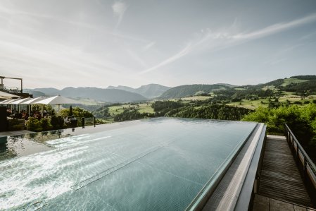 Außenansicht des Hotel Bergkristalls - Mein Resort im Allgäu in Oberstaufen im Sommer mit Blick auf den Außenpool und einen Teil des Hotelgebäudes
