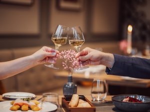 Ansicht eines Abendessen und zwei Weingläser, mit denen angestoßen wird im AMERON Neuschwanstein Alpsee Resort & Spa in Hohenschwangau