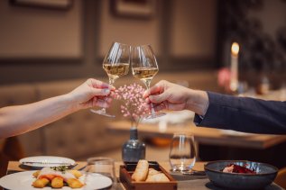 Ansicht eines Abendessen und zwei Weingläser, mit denen angestoßen wird im AMERON Neuschwanstein Alpsee Resort & Spa in Hohenschwangau