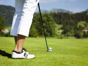 Ansicht von Beinen einer Golfspielerin, einem Schläger und einem Ball auf einem Golfplatz.