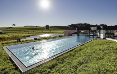Ansicht des Outdoorpools des Haubers Naturresort in Oberstaufen im Sommer. Eine Person schwimmt darin.
