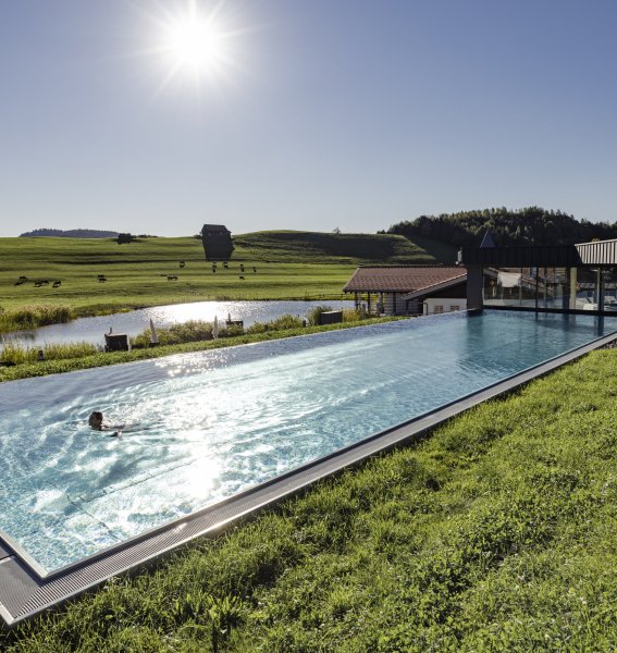 Ansicht des Outdoorpools des Haubers Naturresort in Oberstaufen im Sommer. Eine Person schwimmt darin.