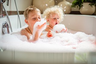 Es sind zwei Kinder in einer Badewanne des Hotel Franks in Oberstdorf zu sehen, die lachen und mit dem Badeschaum spielen.