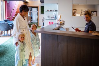 Es ist eine Mutter mit ihren beiden Kindern im Arm zu sehen, die an der Theke im Wellnessbereichs des Hotel Franks in Oberstdorf stehen.