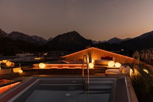 Es ist die Dachterrasse des Hotel Franks in Oberstdorf zu sehen bei Dämmerung und Bergkulisse.