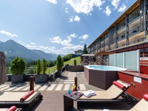 Außenansicht vom Allgäuhotel Tanneck in Fischen mit Blick auf Liegestühle und einen Whirlpool sowie die Umgebung.