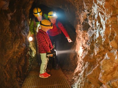 Es sind zwei Erwachsene Personen und ein Kind mit Taschenlampen in den Erzgruben Burgberg zu sehen.