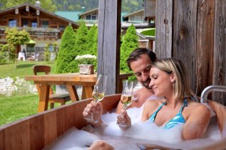 Es ist ein Paar mit zwei Sektgläsern im Whirlpool des Alpin Chalets in Oberjoch im Sommer zu sehen.