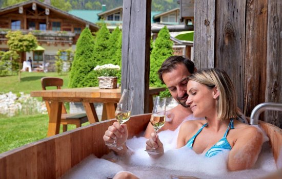Es ist ein Paar mit zwei Sektgläsern im Whirlpool des Alpin Chalets in Oberjoch im Sommer zu sehen.