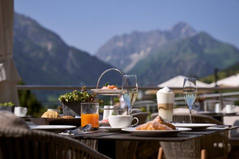 Es ist ein Tisch mit Frühstück darauf zu sehen auf der Terrasse des Travel Charme Ifen Hotel im Kleinwalsertal