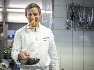 Es ist der Küchenchef Sven des Hotel Franks in Oberstdorf zu sehen, der gerade eine Pfanne in der Hand hält und mit dieser Karotten in die Luft wirft.