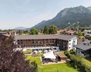 Es ist das Hotel Exquisit in Oberstdorf von außen im Sommer zu sehen mit Bergen im Hintergrund.