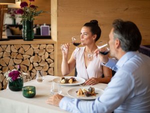 Es ist ein Paar zu sehen, welche gerade beim Abendessen im Restaurant des Hotels Exquisit in Oberstdorf sitzen und aus ihrem Weinglas trinken.