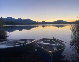 Ansicht des Hopfensees mit Bergkulisse, im Vordergrund sind kleine Boote zu sehen