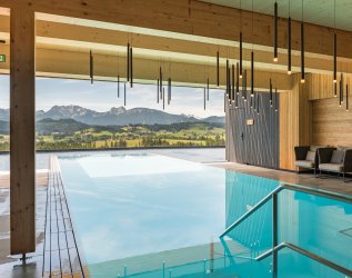 Bild des Infinitypools des Hotels mit Blick ins Grüne und auf die Berge im Allgäu.