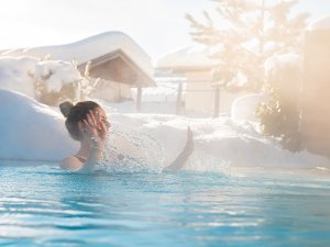 Eine Frau genießt umgeben vom Schnee die Wärme im Außenpool im Freiberg das Romantik Hotel in Oberstdorf