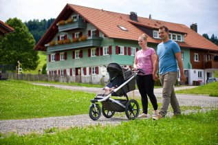Eine Familie spaziert während ihres Urlaub im Ferienhotel Starennest in Oberstaufen mit dem Kinderwagen durch die Umgebung