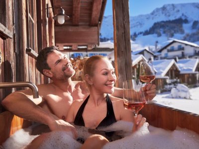Es ist ein Paar mit zwei Weingläsern im Whirlpool des Alpin Chalets in Oberjoch im Winter zu sehen