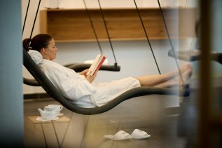 Eine Frau liegt im Bademantel in einer der Hängeliegen im Wellnessbereich im Hotel Bannwaldsee in Halblech und liest ein Buch