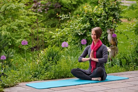 Eine Frau im Diana Naturpark Hotel in Oberstaufen macht draußen auf einer Matte Yoga während um sie herum der Garten grün blüht