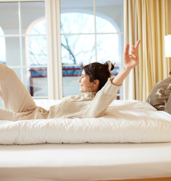 Eine Frau lässt sich auf ein Doppelbett im Hanusel Hof in Weitnau fallen