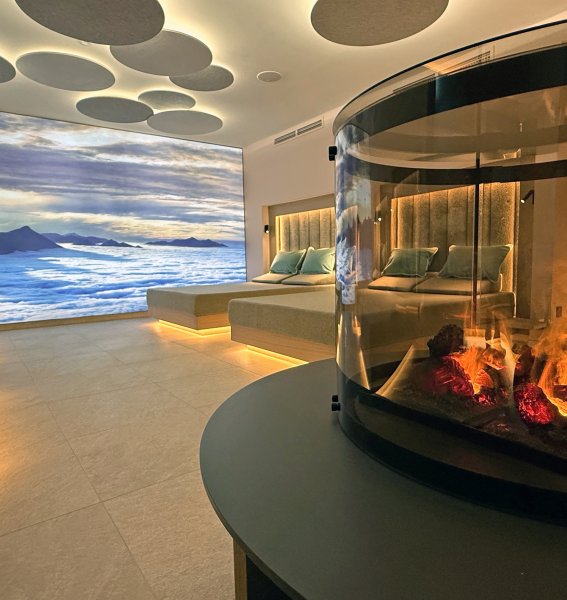 Neuer Ruheraum im Wellnessbereich des Bayerischen Hofs in Oberstaufen mit Blick auf ein Bergpanoramabild und einen Kamin mit Feuer.