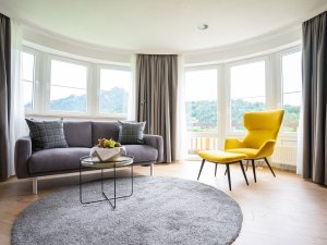 Einblick in eines der Zimmer im Best Western Plus Hotel Alpenhof in Oberstdorf mit Blick auf eine Sitzgelegenheit mit Sofa und Sessel sowie der Fensterwand und Ausblick auf die Umgebung