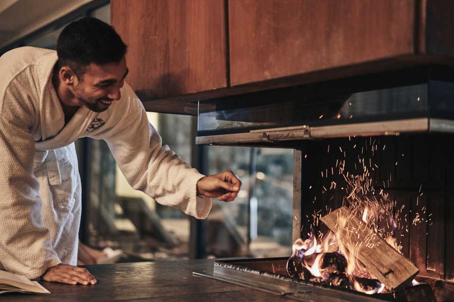 Ifen Hotel Kleinwalsertal Kamin Ein Mann beugt sich zum brennenden Kamin im Ifen Hotel Kleinwalsertal hinunter