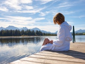 Eine Frau genießt im Bademantel das schöne Wetter auf dem Steeg des Sees in der Nähe des Biohotels Eggensberger in Füssen, Hopfen am See