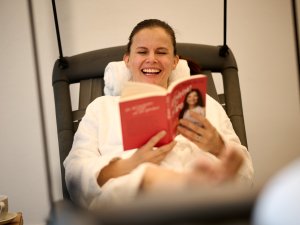 Eine Person liegt auf einer Liege im Wellnessbereich des Hotel Bannwaldsee in Halblech und liest ein Buch