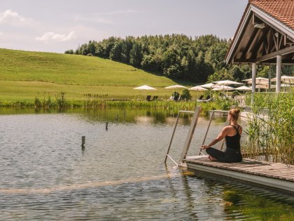 Eine Frau macht am See vom Haubers Naturresort in Oberstaufen umgeben von grünen Wiesen Yoga