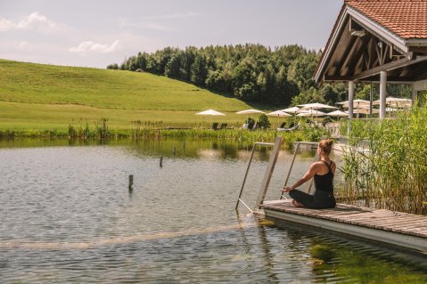 Eine Frau macht am See vom Haubers Naturresort in Oberstaufen umgeben von grünen Wiesen Yoga