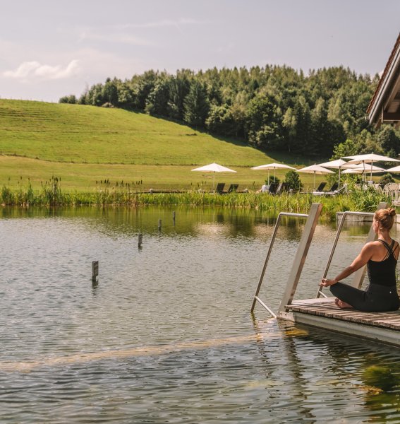 Eine Frau macht am See vom Haubers Naturresort in Oberstaufen umgeben von grünen Wiesen Yoga