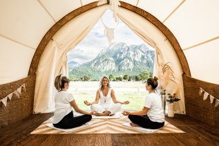 Drei Frauen sitzen in einem Zelt im Hotel Das Rübezahl in Schwangau und machen Yoga