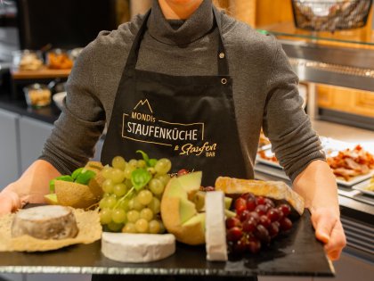 Ein Mitarbeiter im MONDI Resort Oberstaufen in Oberstaufen trägt eine Platte mit Käsevariationen und Trauben
