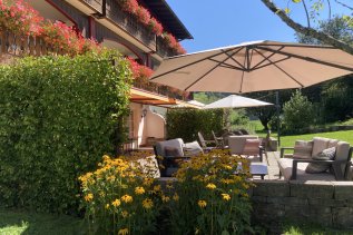 Außenansicht des Hotels Mühlenhof in Oberstaufen im Sommer mit Blick auf die Terrasse und den blühenden Garten