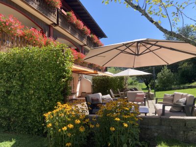 Außenansicht des Hotels Mühlenhof in Oberstaufen im Sommer mit Blick auf die Terrasse und den blühenden Garten