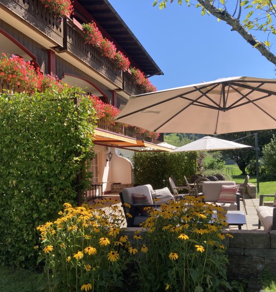 Außenansicht des Hotels Mühlenhof in Oberstaufen im Sommer mit Blick auf die Terrasse und den blühenden Garten