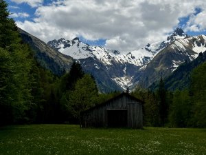 Lichtung umgeben von bewälderten Bergen und verschneiten Bergketten mit einer Hütte in der Mitte der Wiese als beliebtes Ziel von Gästen im Best Western Plus Hotel Alpenhof in Oberstdorf
