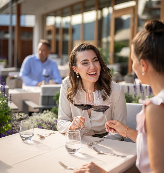 Zwei Frauen stoßen mit einem Glas Rotwein auf der Terrasse des Restaurants im Hotel Exquisit in Oberstdorf an.