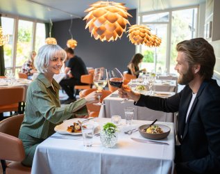 Ein Paar genießt das Essen bei einem Glas Wein im Das Freiberg Romantik Hotel in Oberstdorf.