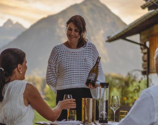 Die Gastgeberin des Hotels Kühberg in Oberstdorf serviert Gästen auf der Terrasse eine Flasche Wein.