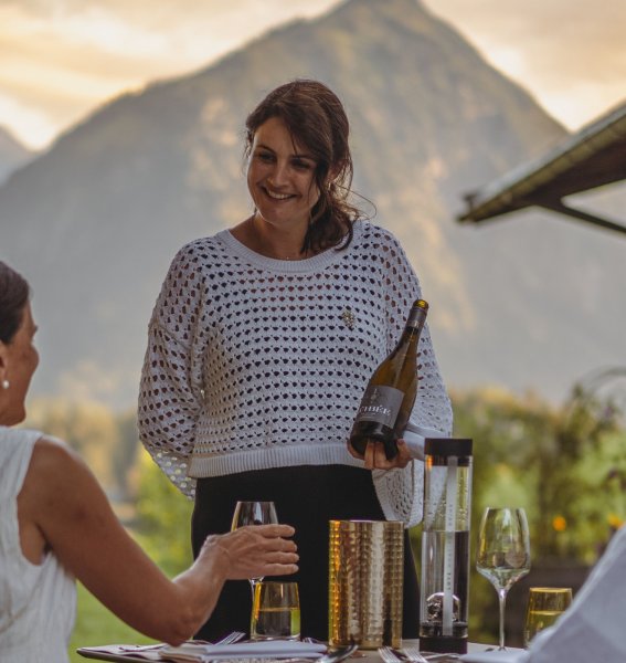 Die Gastgeberin des Hotels Kühberg in Oberstdorf serviert Gästen auf der Terrasse eine Flasche Wein.