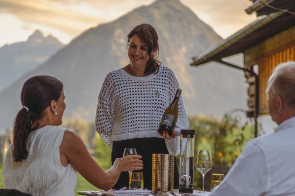 Die Gastgeberin des Hotels Kühberg in Oberstdorf serviert Gästen auf der Terrasse eine Flasche Wein.