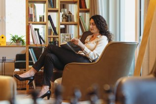 Eine Dame ließt ein Buch in der Lobby neben dem Bücherregal im Hotel Kühberg in Oberstdorf.