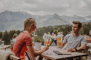Gäste genießen einen Aperitif auf der Terrasse der Alpe Dornach in Oberstdorf.
