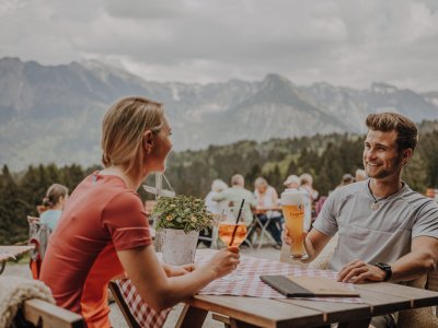 Gäste genießen einen Aperitif auf der Terrasse der Alpe Dornach in Oberstdorf.