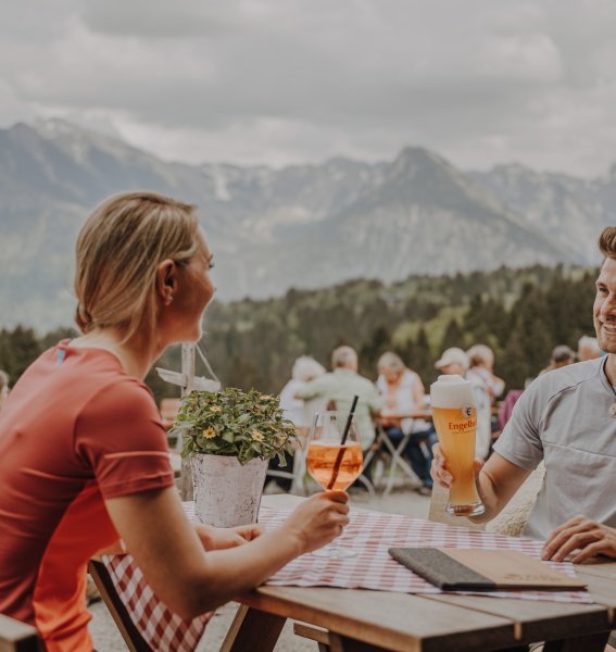 Gäste genießen einen Aperitif auf der Terrasse der Alpe Dornach in Oberstdorf.